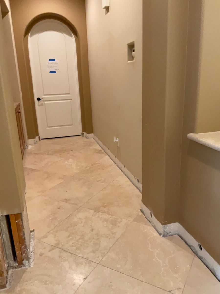 Hallway with beige tile floor, tan walls, a white door, and exposed wall studs.