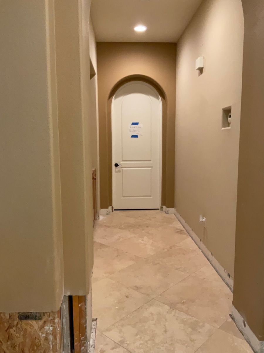 Narrow hallway with off-white walls, arched doorway with white door, and beige tile flooring.