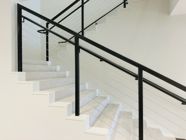 White staircase with black metal railing and cable balusters.
