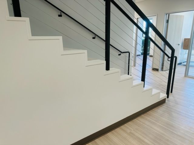 White stairs with black railing, leading to a light wood floor in a modern home.