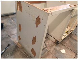 Damaged white cabinet with visible filler patches; in a room with tile flooring.