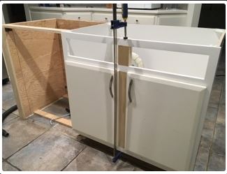 Cabinet installation: wooden frame attached to a white cabinet, held with a clamp, inside kitchen.