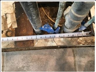 Pipes in floor opening, tape measure across opening. Blue tape around pipes.