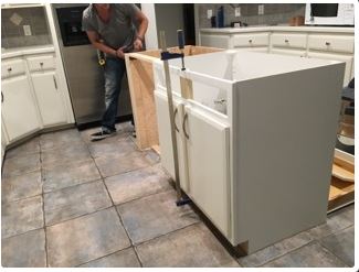Person installing a cabinet in a kitchen with white cabinets and a tile floor.