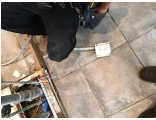 Electrician working on electrical outlet in tiled floor.