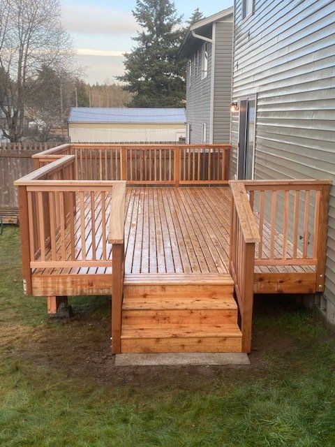 Wooden deck with stairs attached to a two-story house, viewed from the lawn.