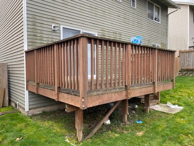 Brown wooden deck attached to a light green house, with a grassy lawn.