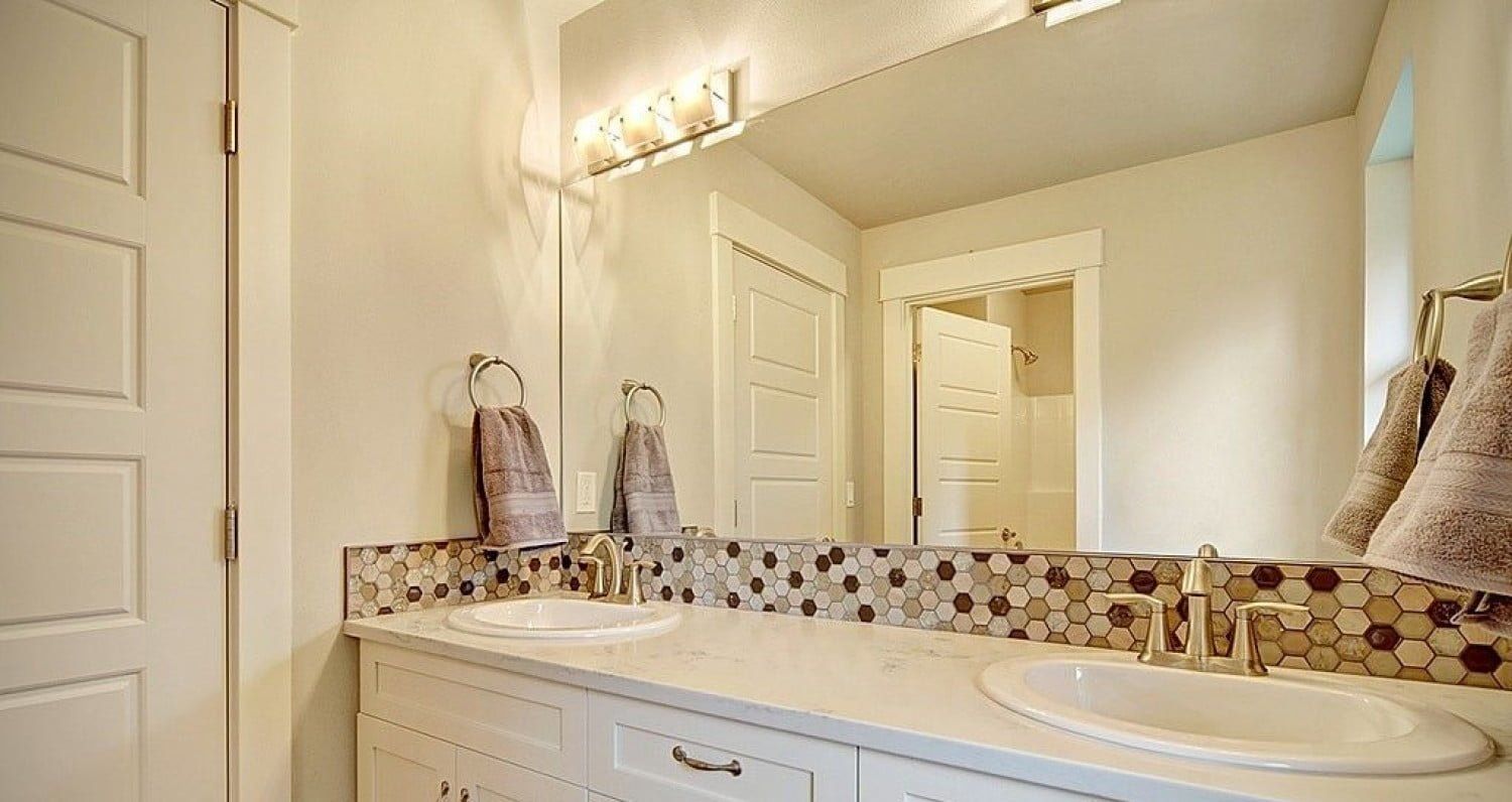 Bathroom with white vanity, double sinks, large mirror, and decorative tile backsplash.