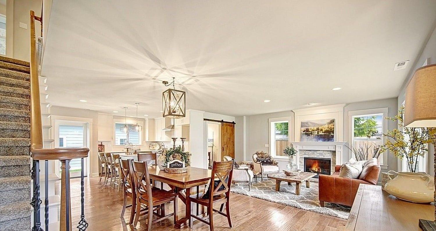 Spacious open-concept living room with dining area, kitchen, and fireplace, hardwood floors, and neutral tones.