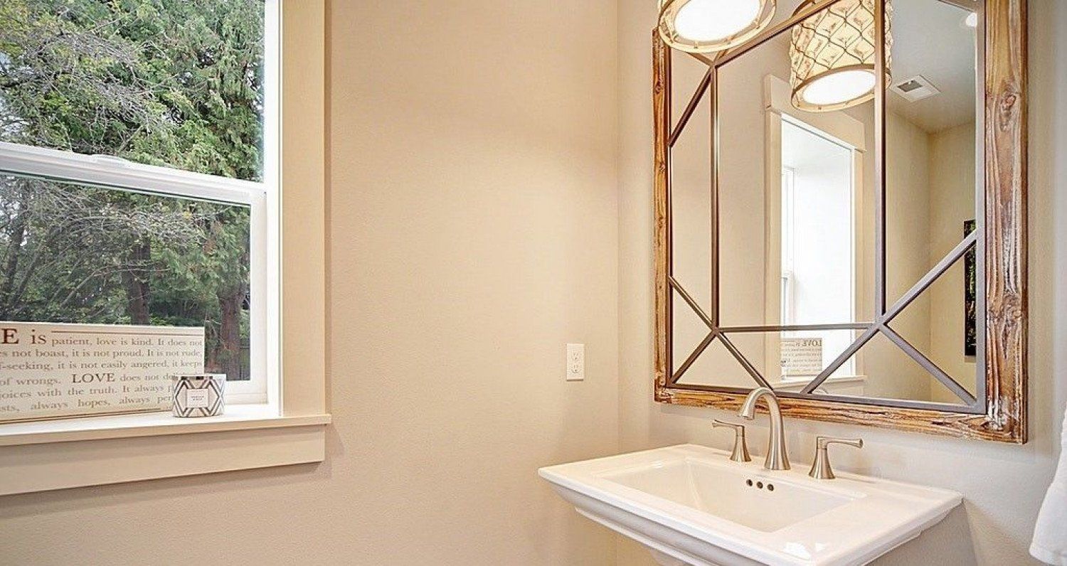 Powder room with a white pedestal sink, large mirror, and window.