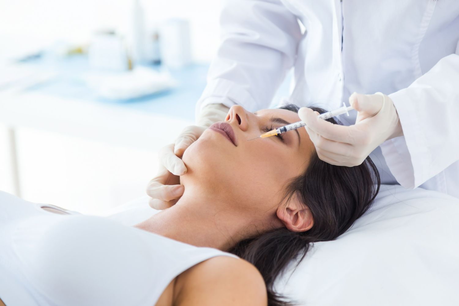 Woman receiving facial injection from a medical professional. White coat, gloved hands, medical setting.