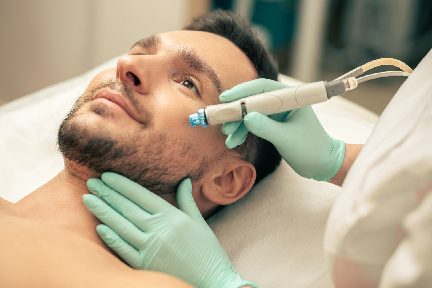 Man receiving a facial treatment. Aesthetican in gloves holds a device to his face.