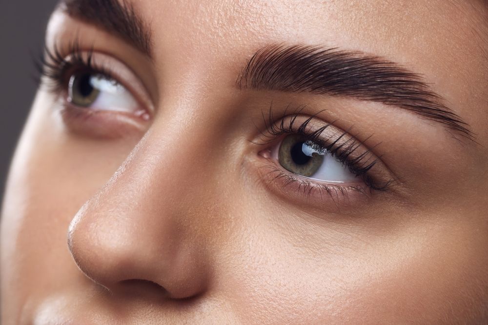 Close-up on a person's eyes and groomed eyebrows, focusing on detailed lashes and natural skin texture.