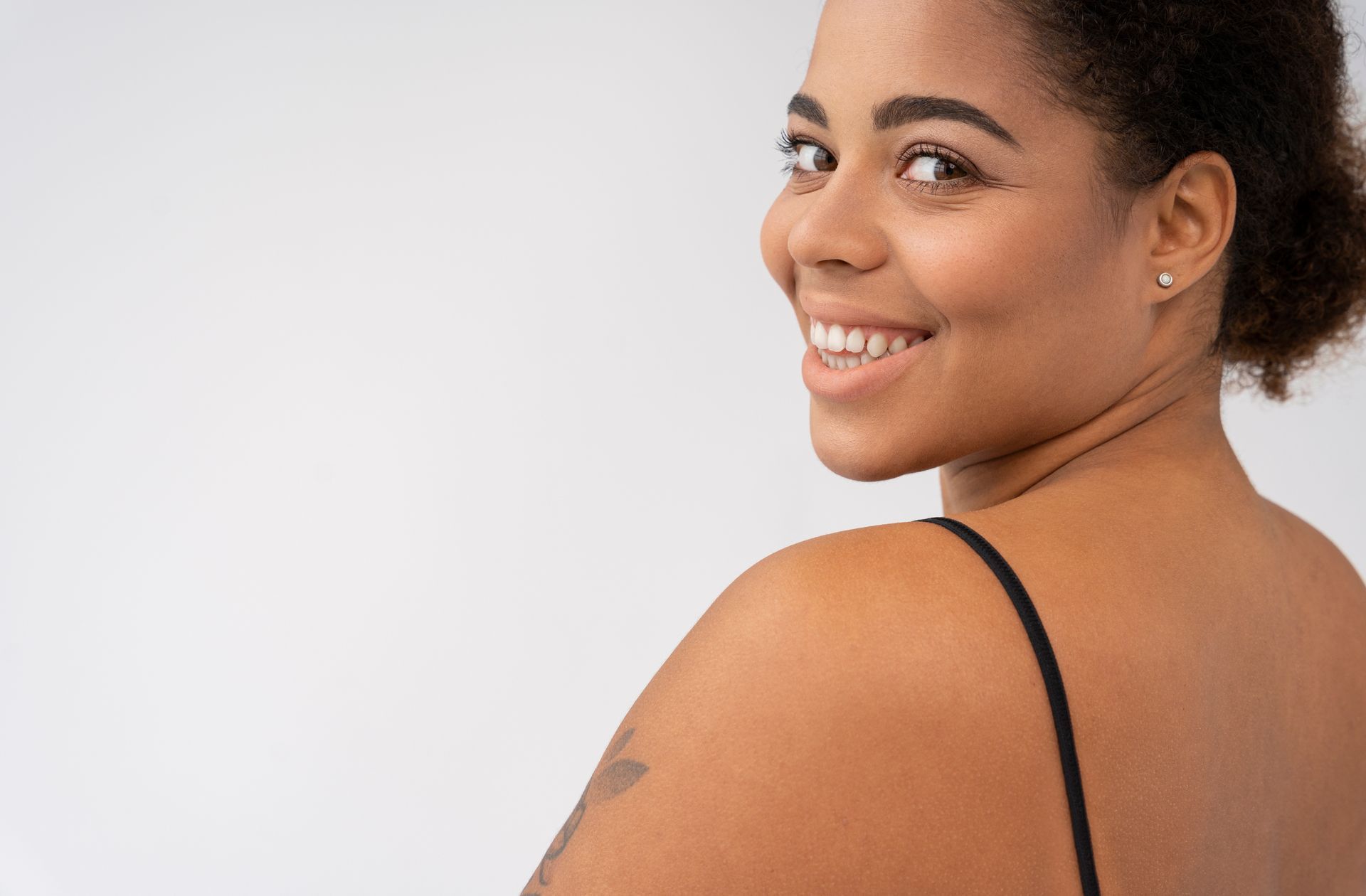 A woman with renewed skin is smiling and looking over her shoulder.