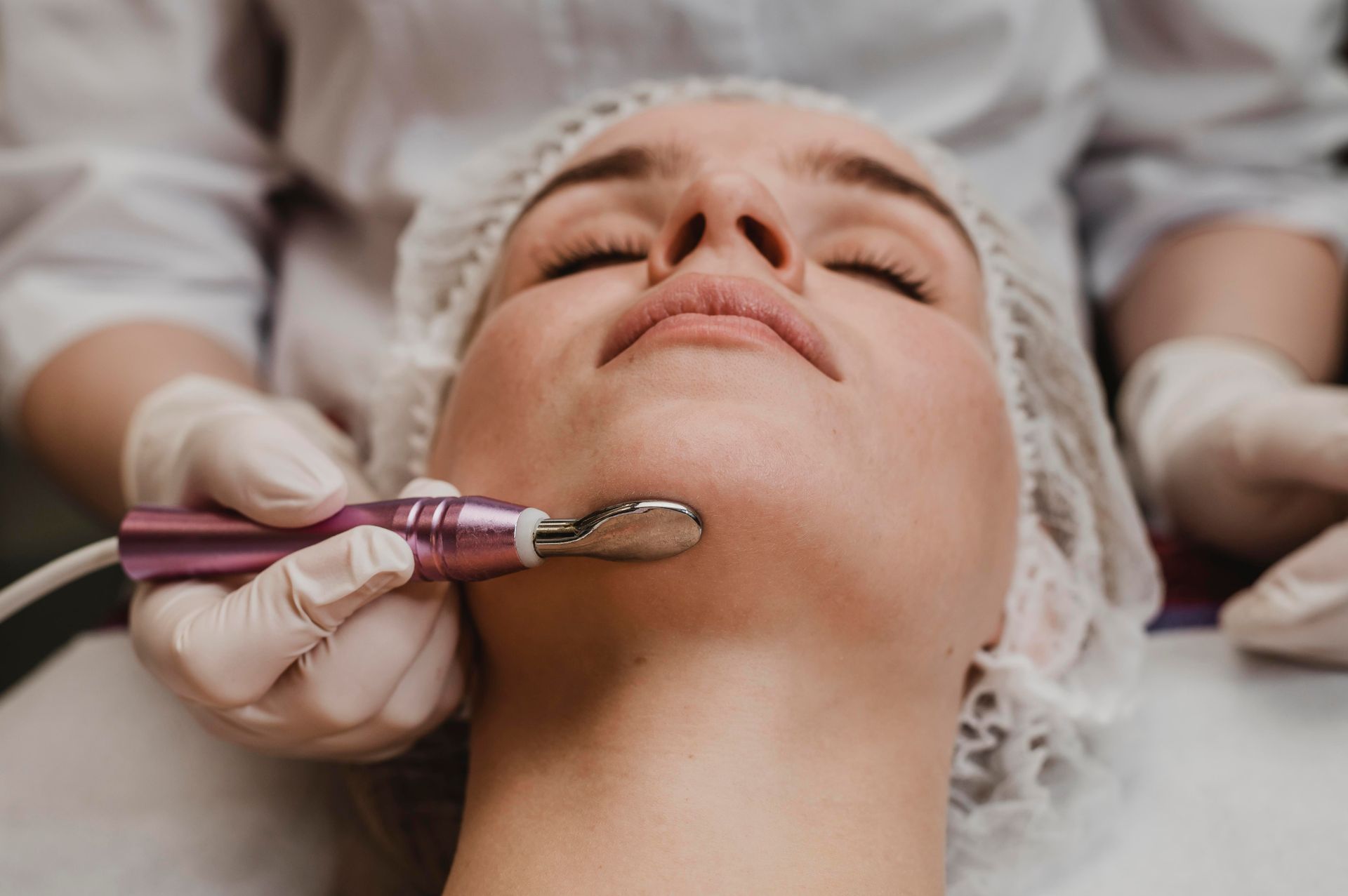 Woman receiving a facial treatment with a handheld device, in a medical setting.
