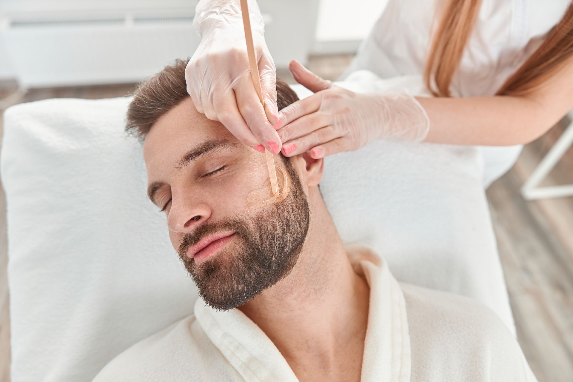 Man getting facial hair waxed at a spa; hands apply wax with a stick.