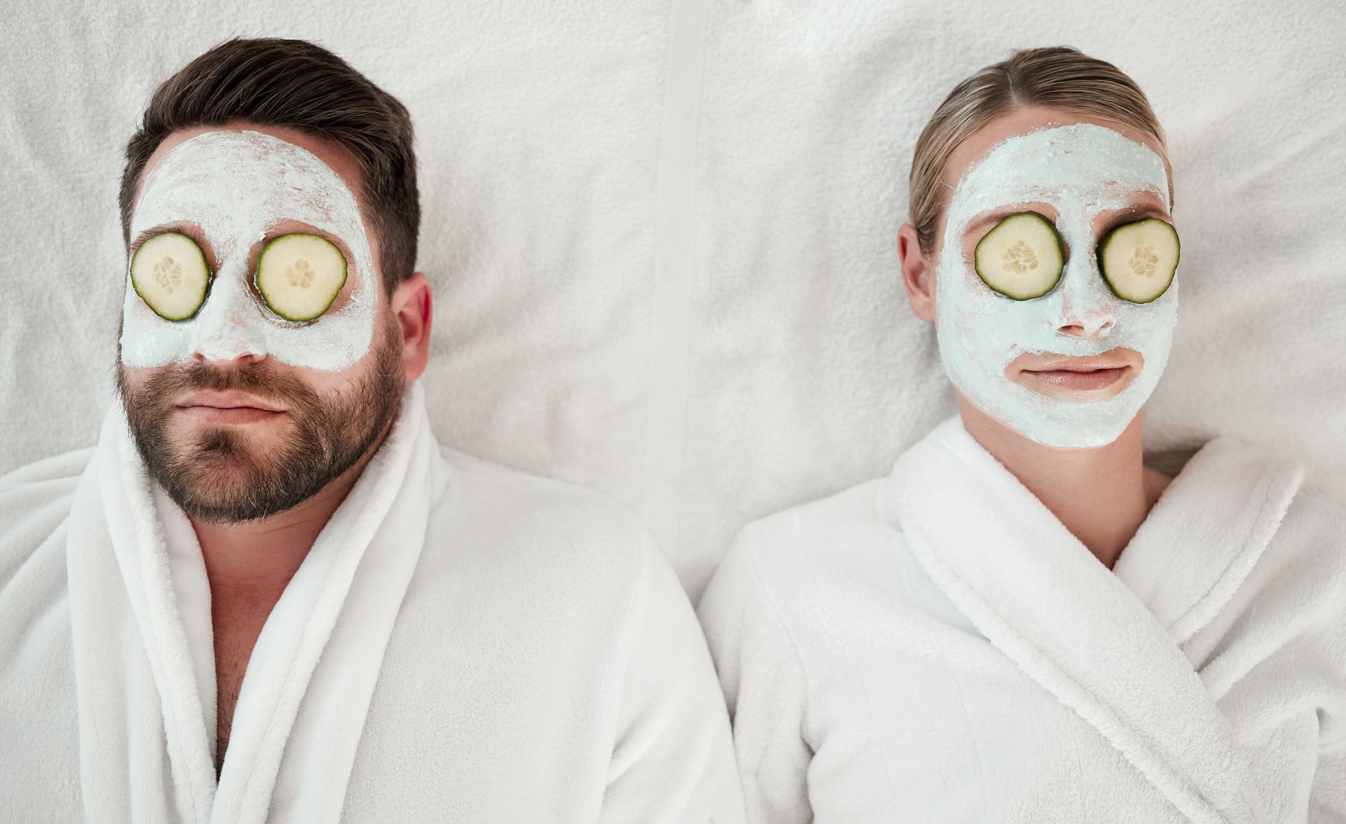 Man and person with face masks and cucumber slices on eyes, wearing robes and relaxing.