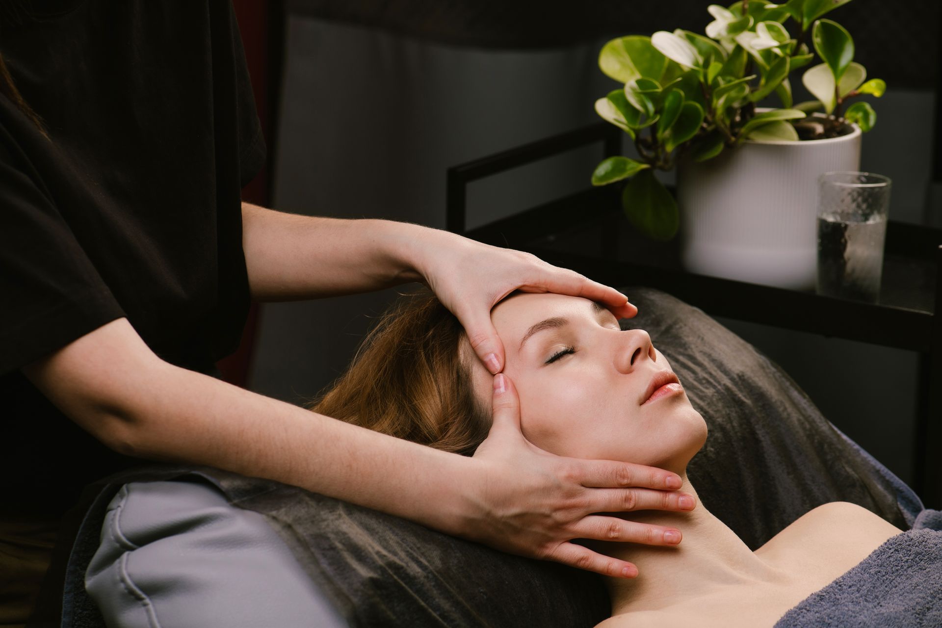 Woman receiving facial massage in spa; hands on forehead, eyes closed.