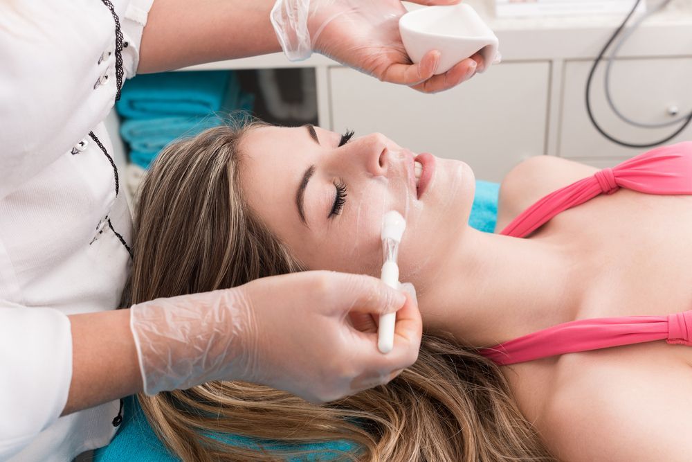 A person receives a facial treatment from a gloved technician, application of product to face.