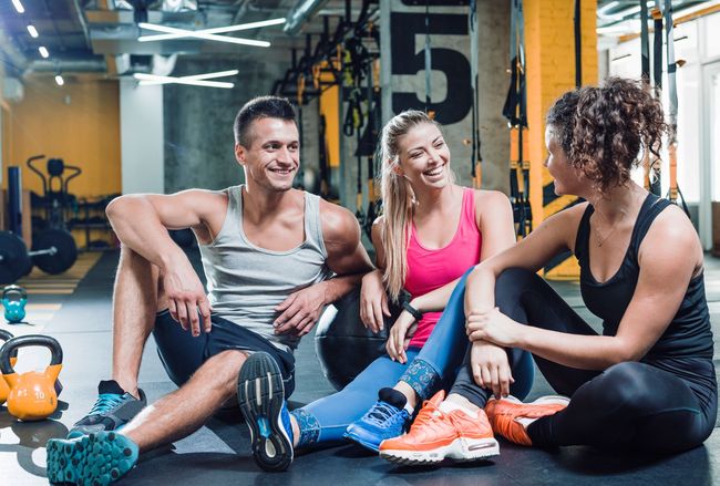 A group of people are sitting on the floor in a gym talking to each other.