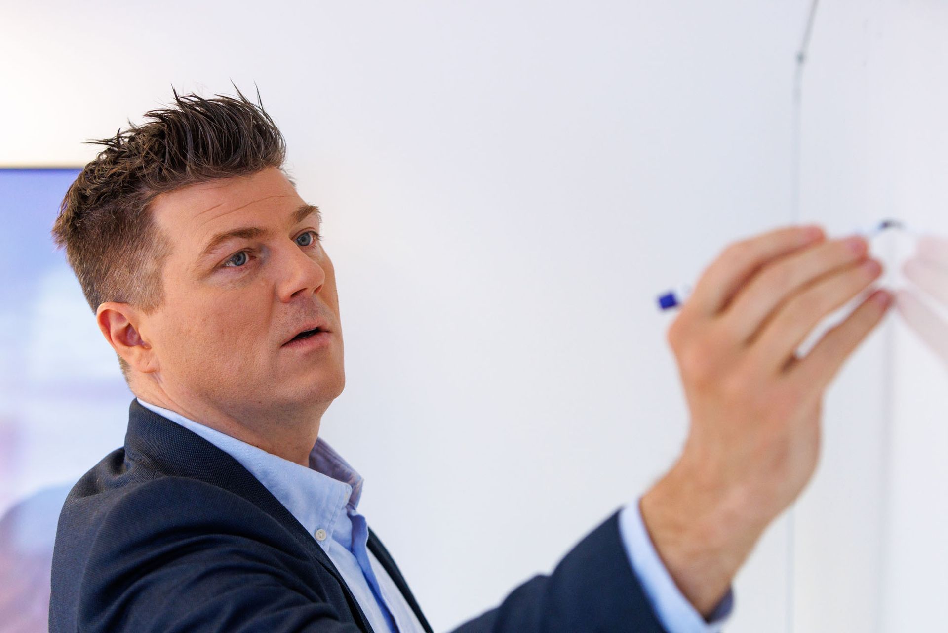 Maður í jakkafötum og bindi skrifar á töflu.