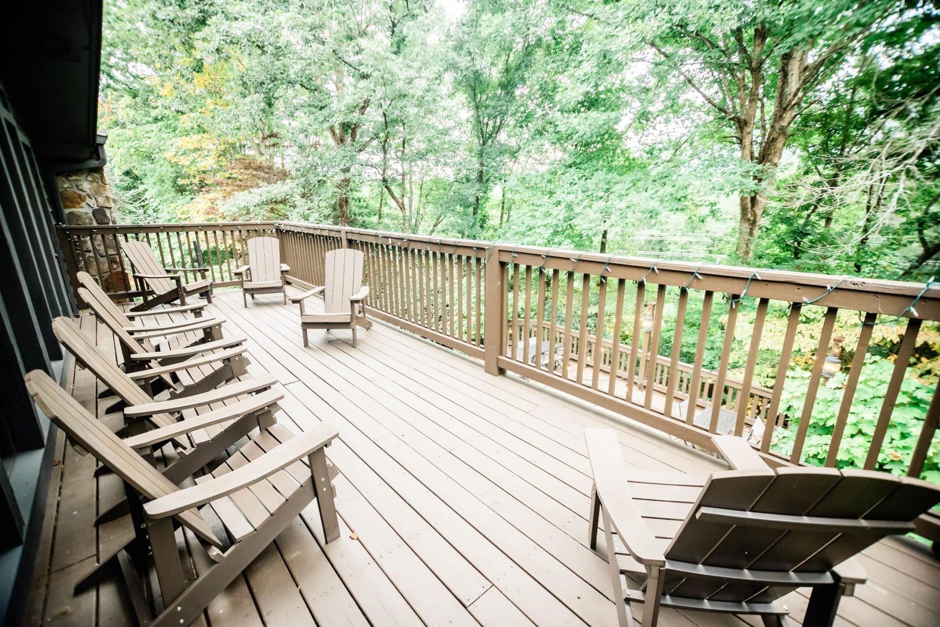 A wooden deck with chairs and a railing surrounded by trees.