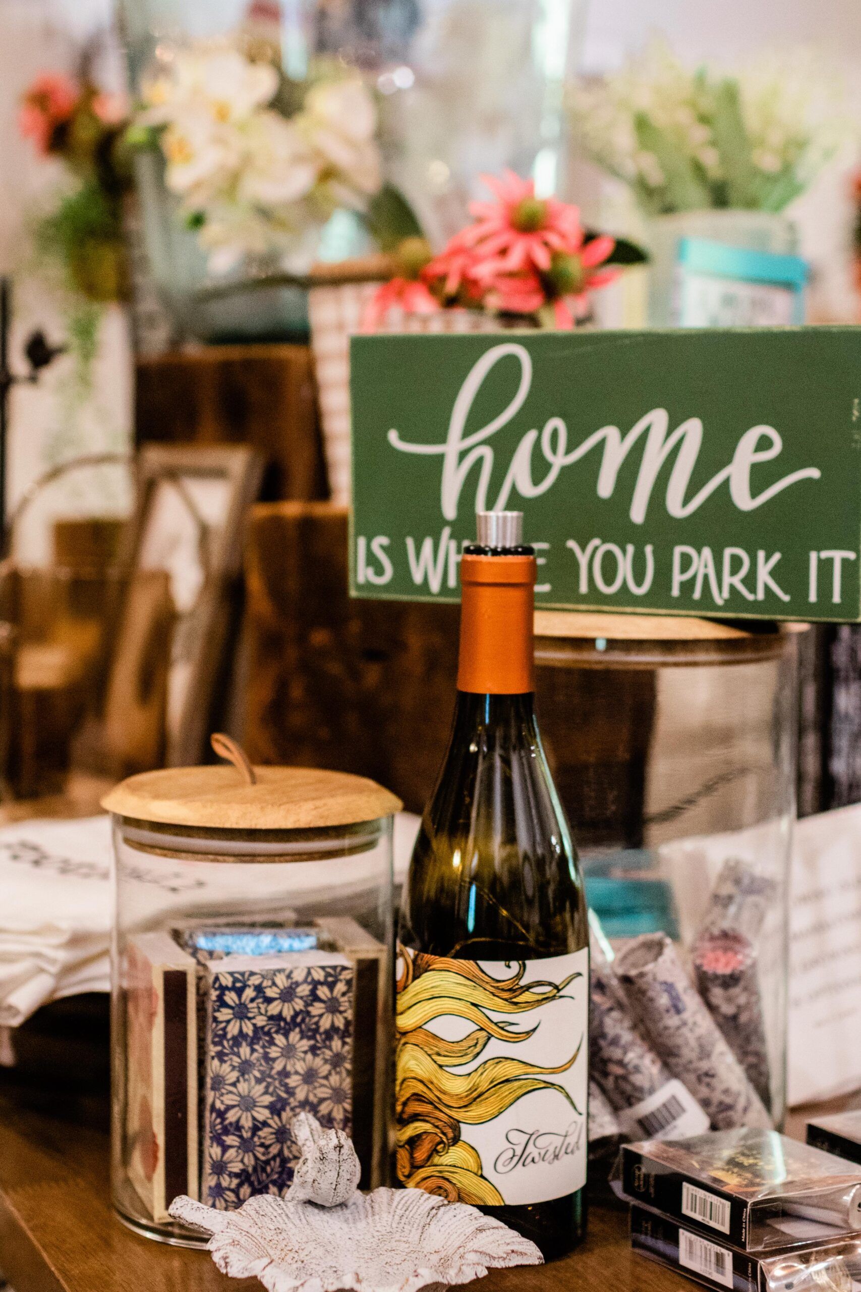 A bottle of wine is sitting on a table next to a sign that says `` home is where you park it ''.