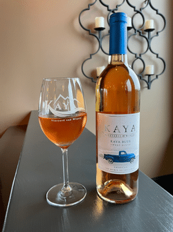 A bottle of kaya wine next to a glass of wine on a table.
