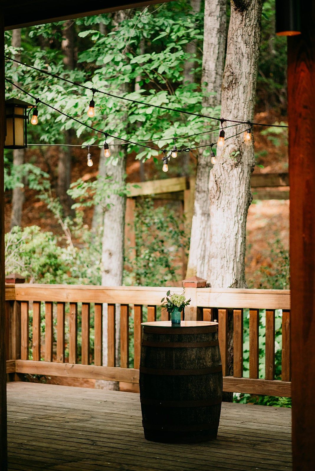 A barrel with a vase of flowers on top of it is sitting on a wooden deck.