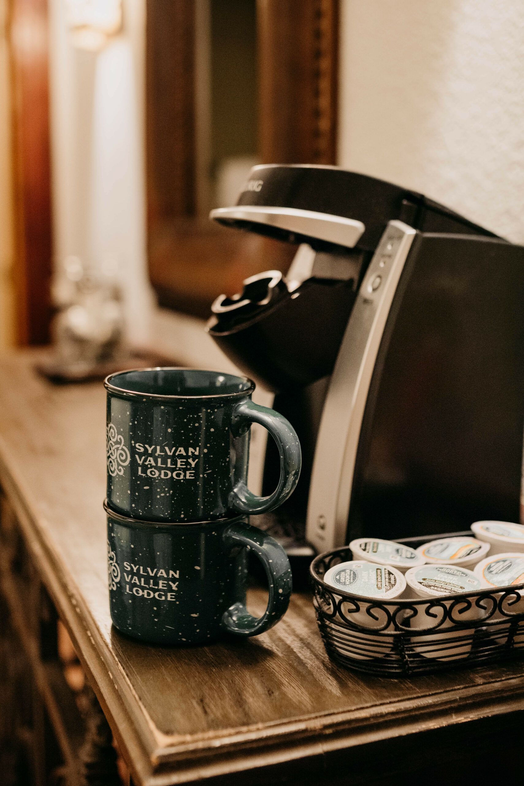 Two mugs are stacked on top of each other on a wooden table next to a coffee maker.