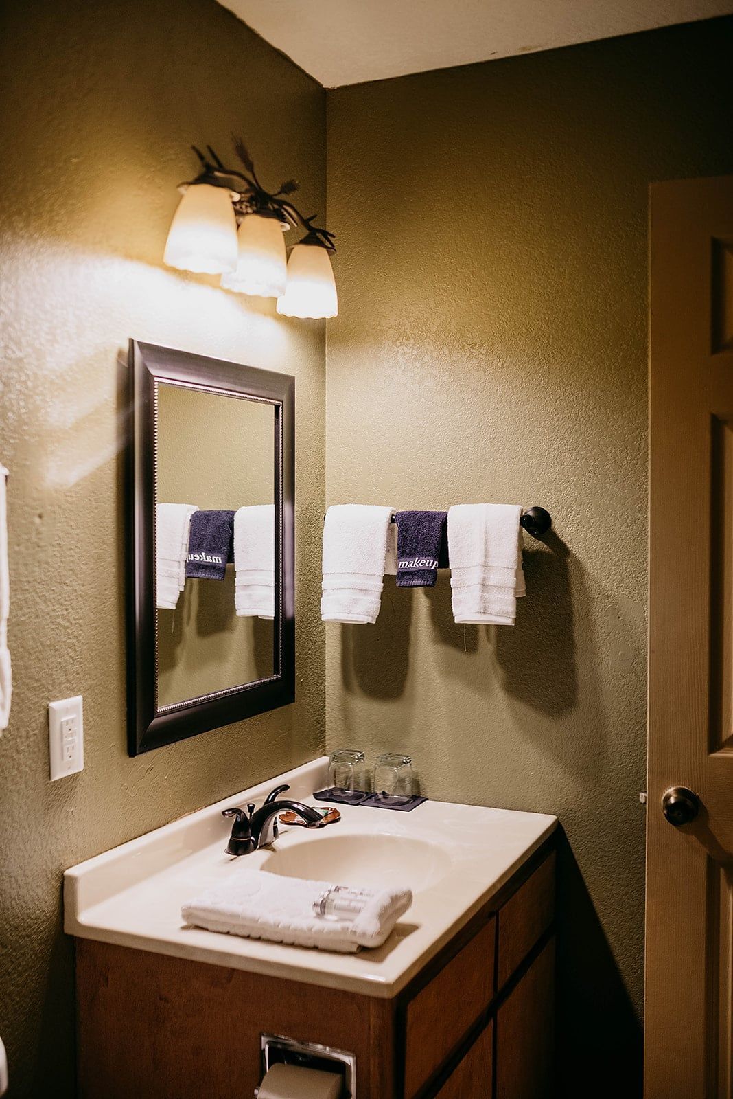 A bathroom with a sink , mirror and towels hanging on the wall.