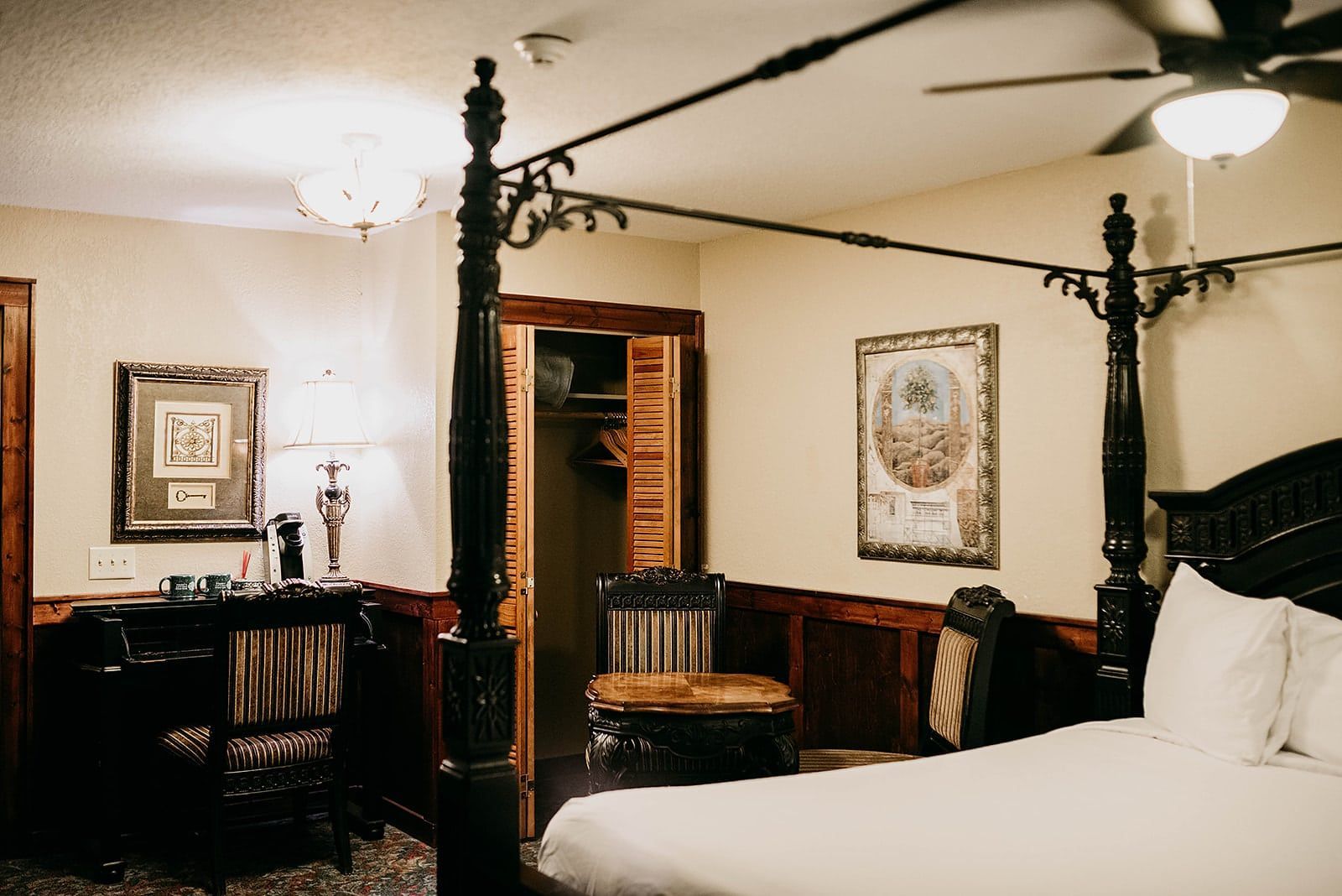 A bedroom with a canopy bed , desk , chair and ceiling fan.