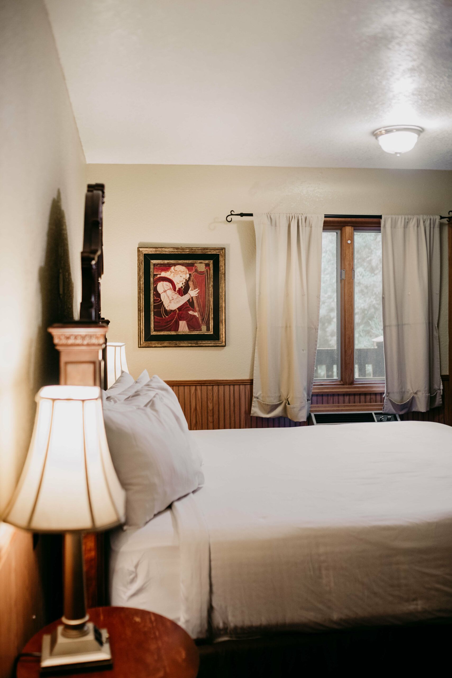 A bedroom with a bed , lamp , nightstand and window.