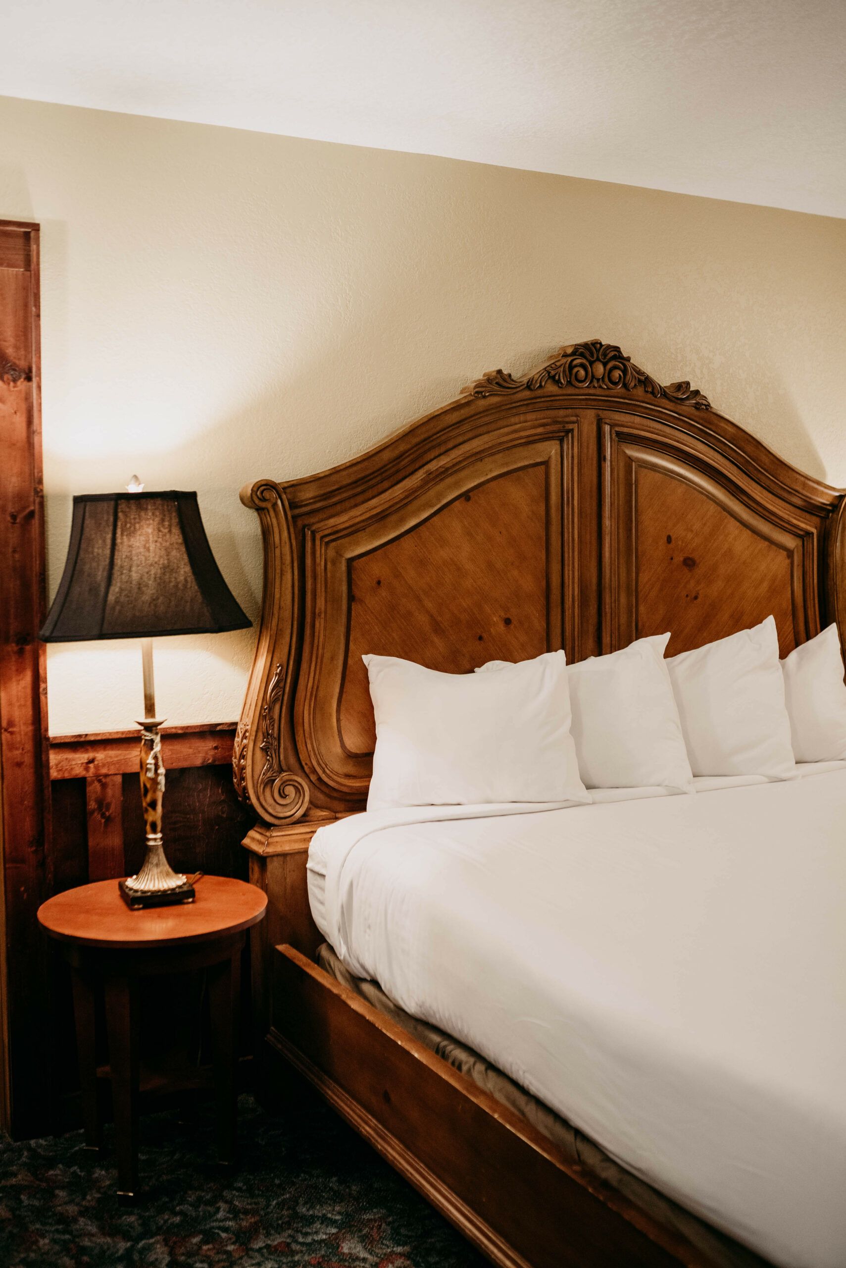 A hotel room with a bed , nightstand , lamp and table.