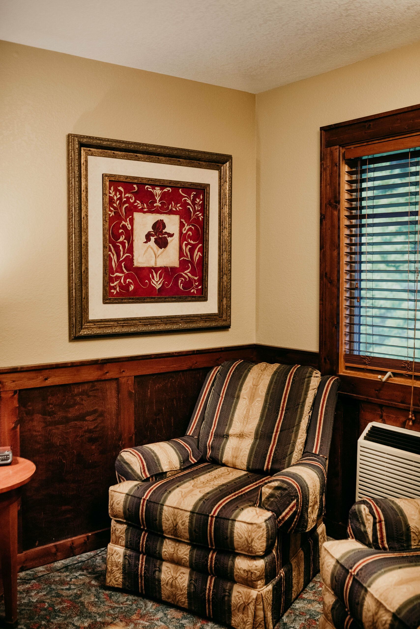 A living room with a striped chair and a picture on the wall.