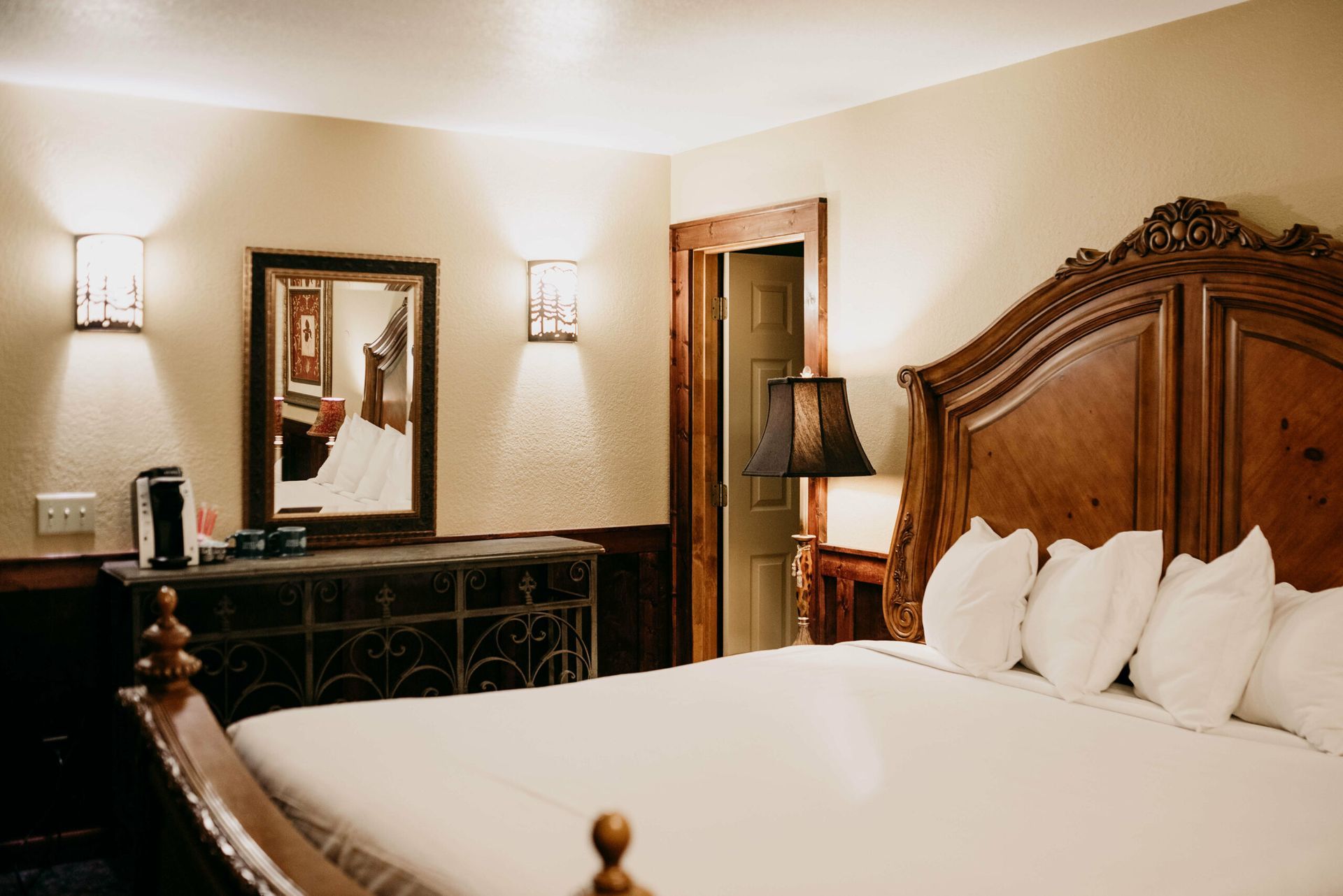 A hotel room with a king size bed , dresser , mirror and lamp.