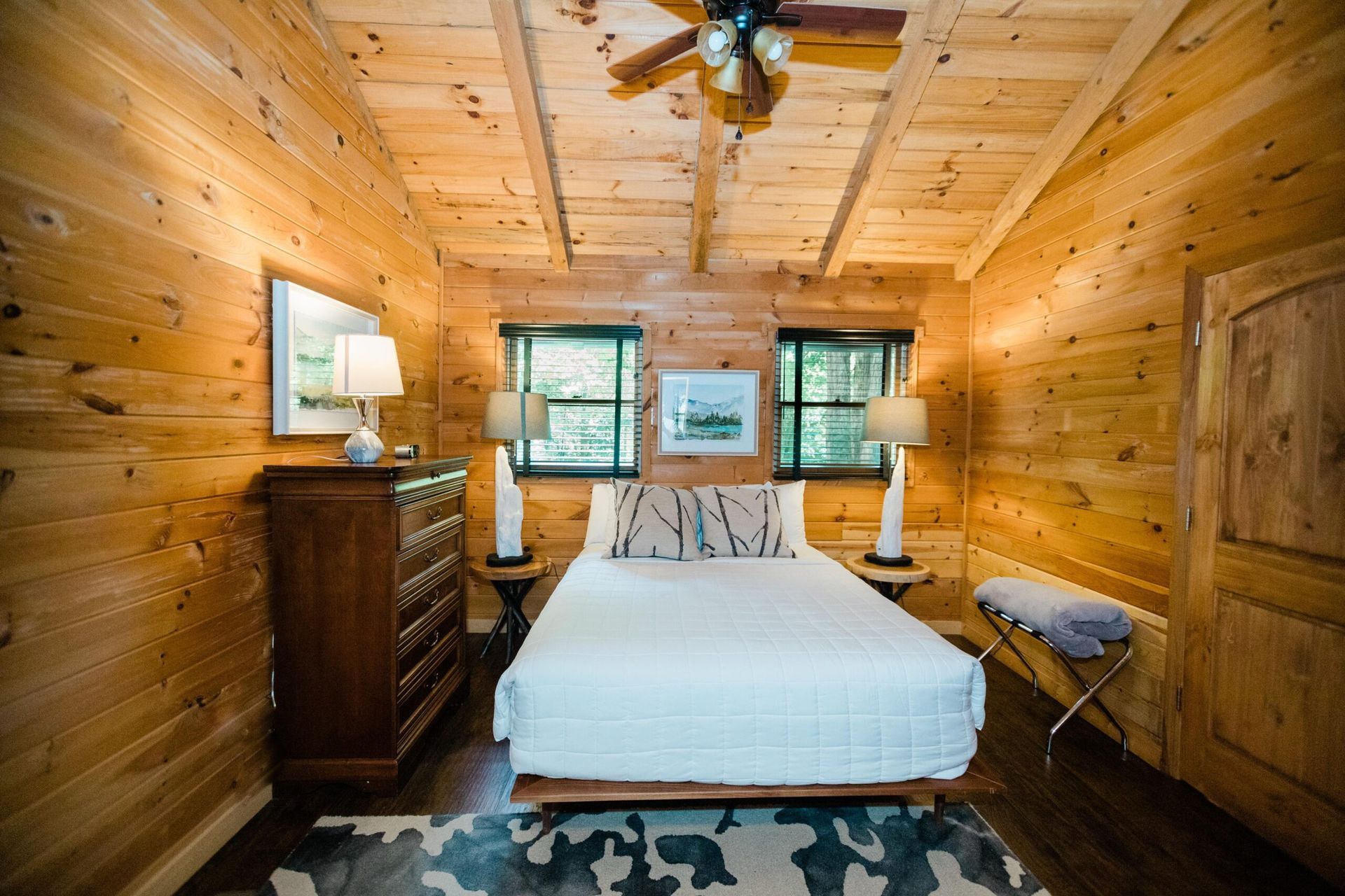 A bedroom in a log cabin with a bed , dresser , and ceiling fan.