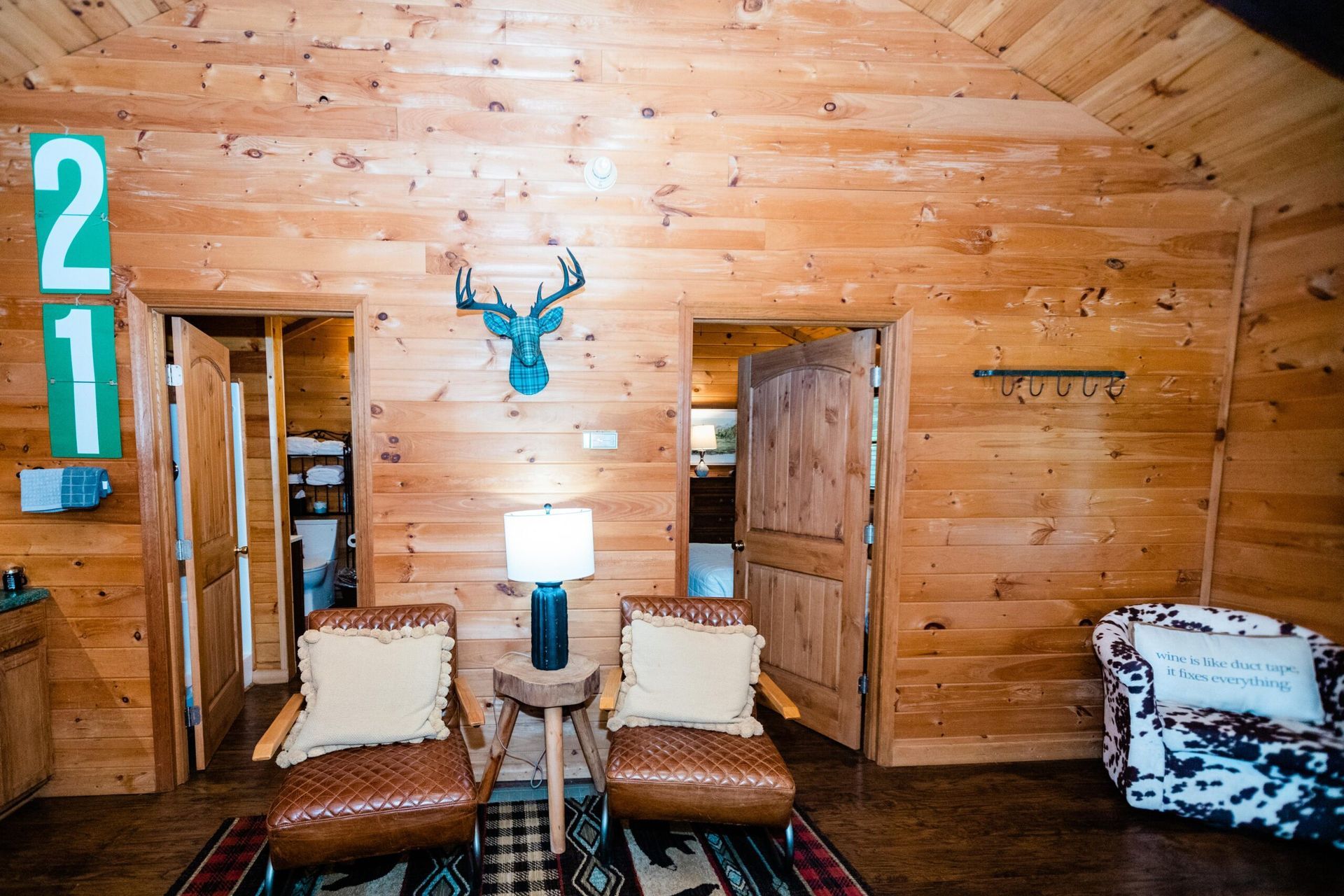 A living room in a log cabin with two chairs and a deer head on the wall.