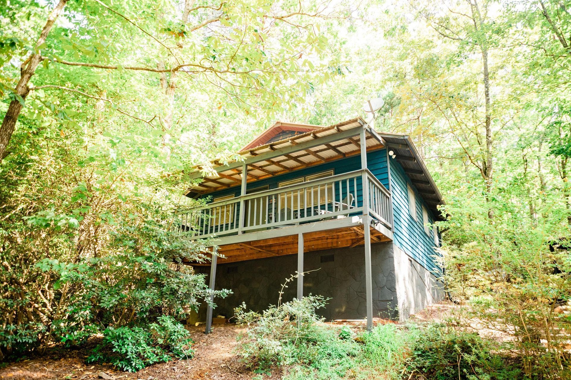 A small blue house with a balcony in the middle of a forest.