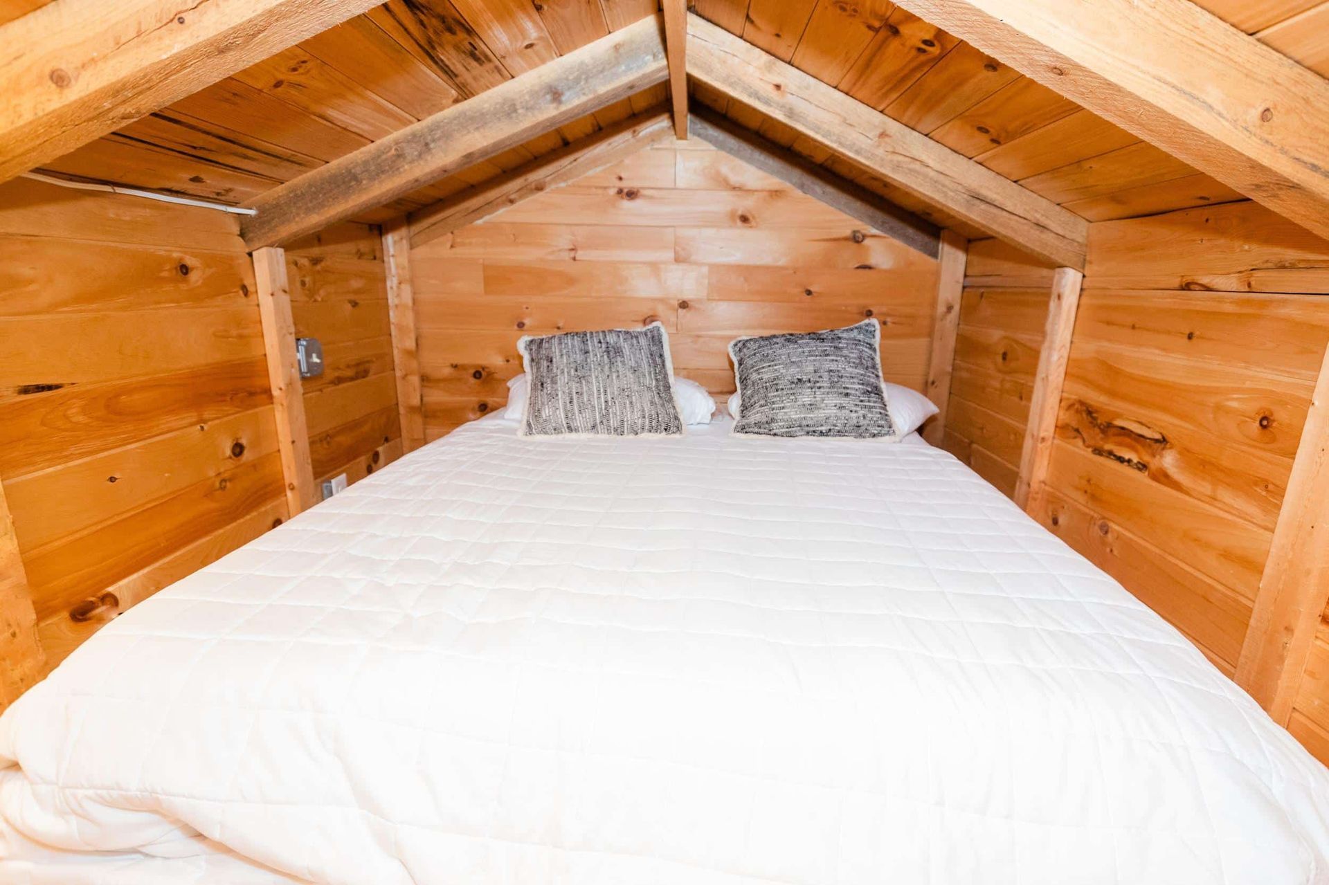 There is a bed in the attic of a wooden cabin.