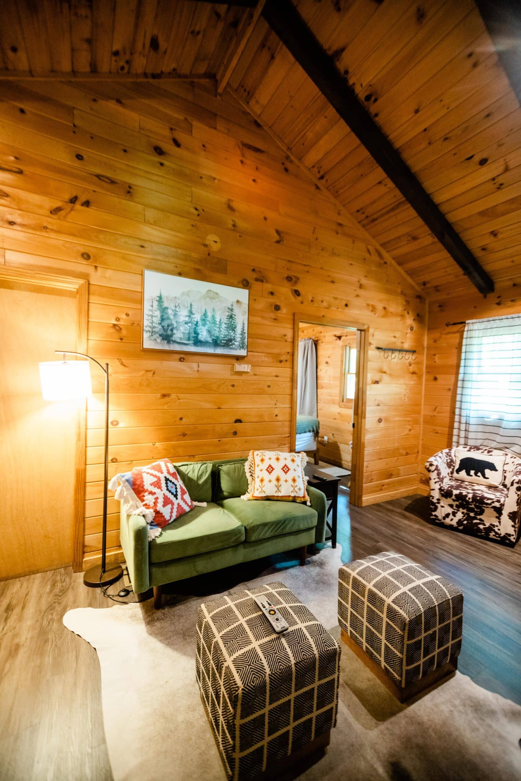 A living room in a log cabin with a green couch and two ottomans.