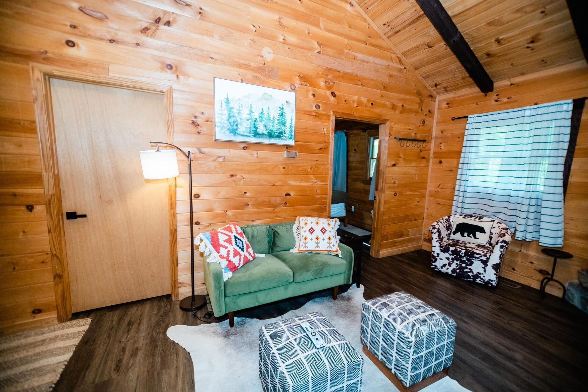 A living room in a log cabin with a green couch and two ottomans.