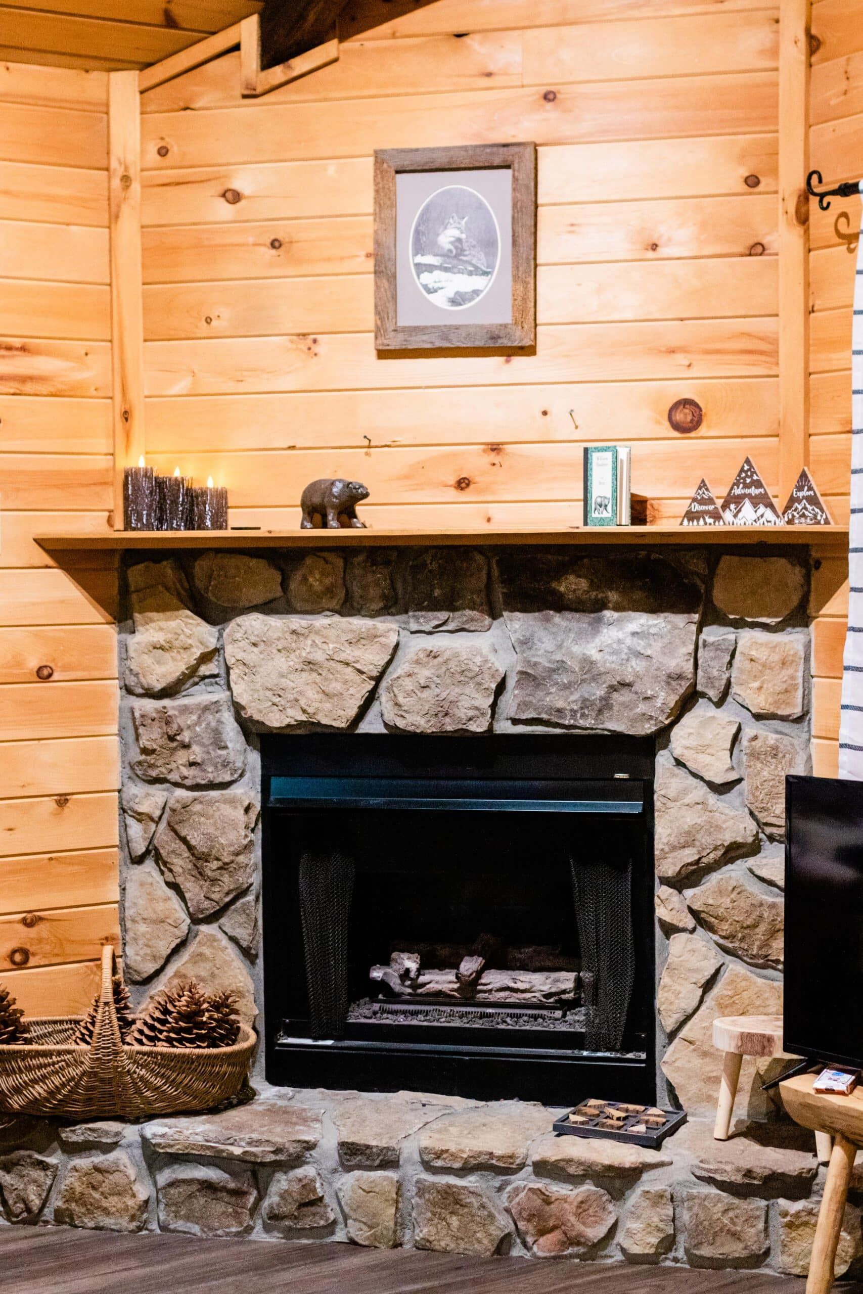 A stone fireplace in a log cabin with a picture on the mantle.
