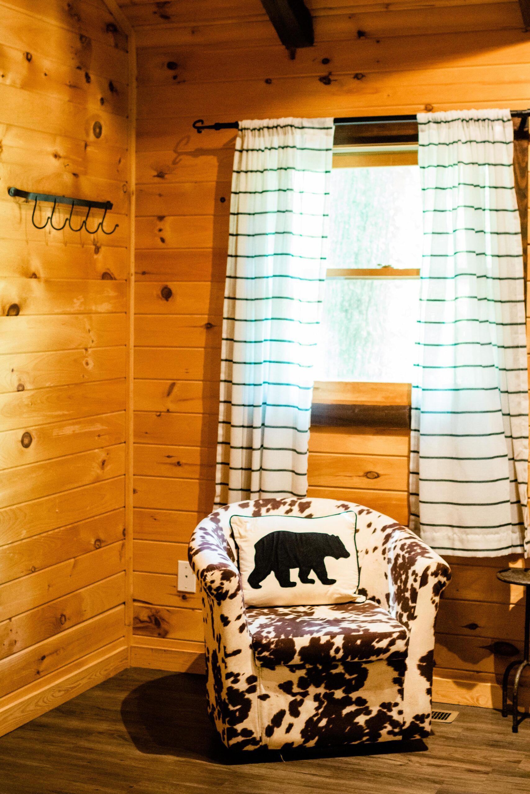 A chair with a bear pillow is sitting in a wooden room next to a window.
