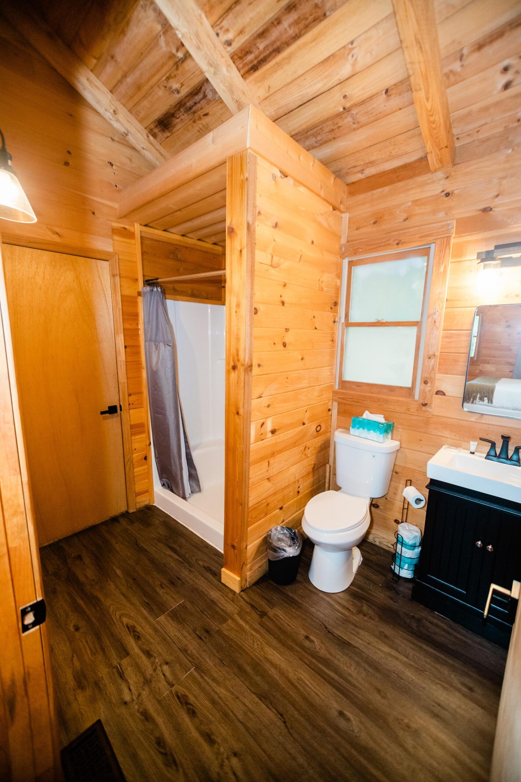 A bathroom in a log cabin with a toilet , sink and shower.
