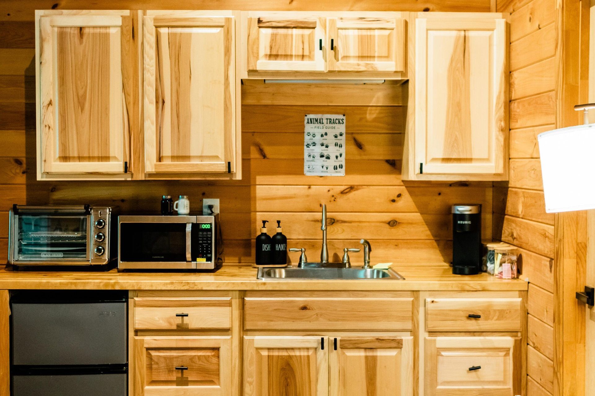A kitchen in a log cabin with wooden cabinets , a sink , microwave , and toaster oven.