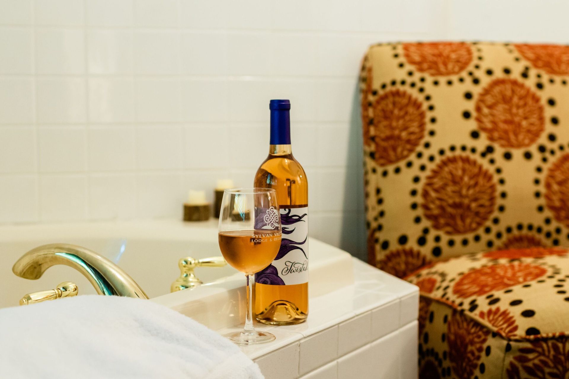 A bottle of wine and a glass of wine are sitting on a bathtub.