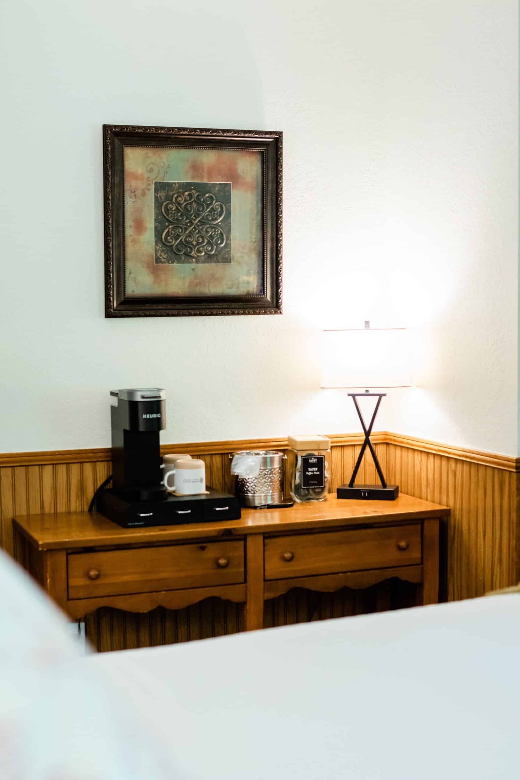 A coffee maker is sitting on a wooden table in a hotel room.
