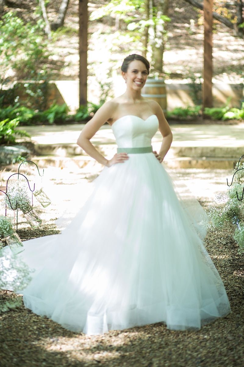 A woman in a white wedding dress is standing in the woods.