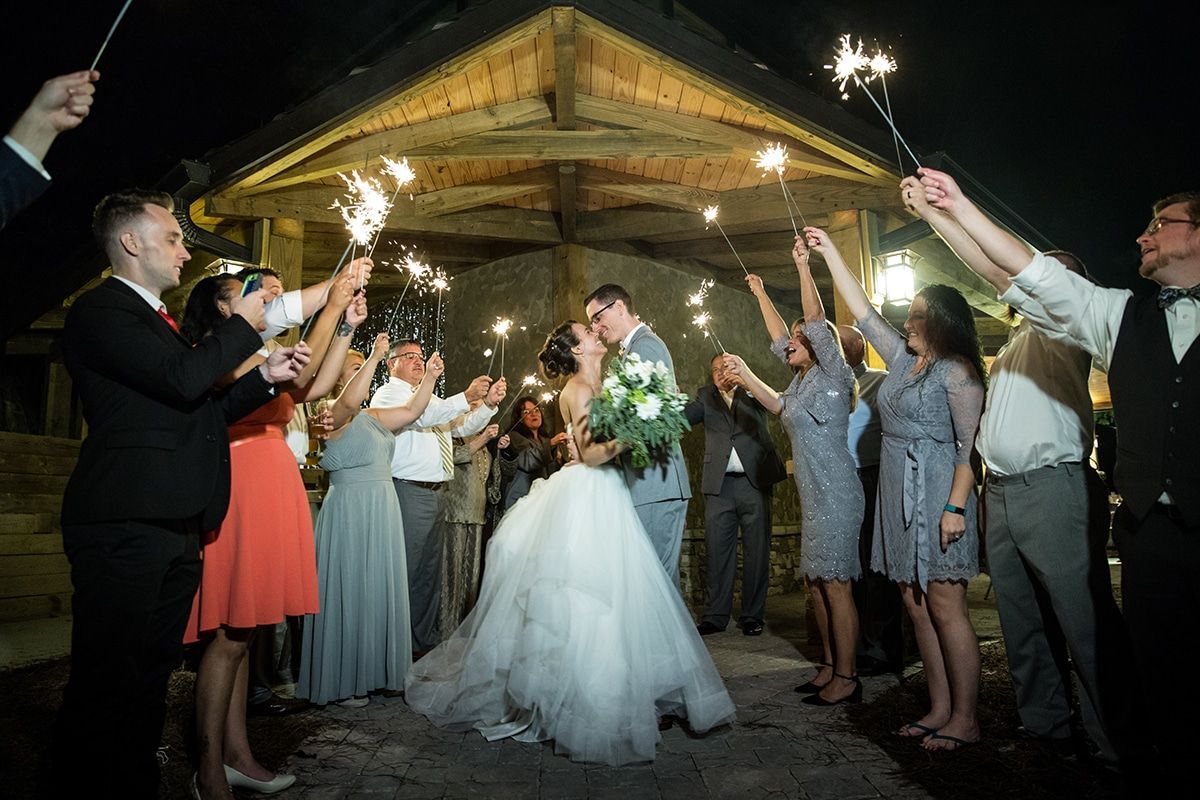 A bride and groom are kissing while their wedding guests hold sparklers.
